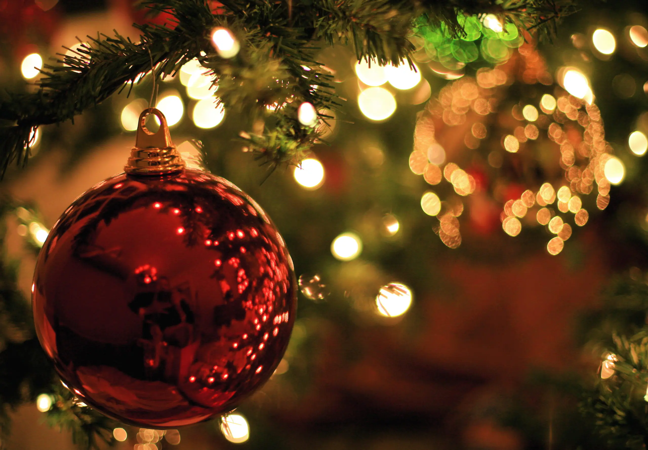 Colour photo of a red Christmas Carols bauble and lights.