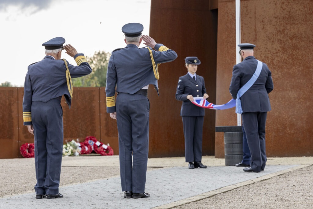 Two men in uniform saluting as the RAF ensign is lowered